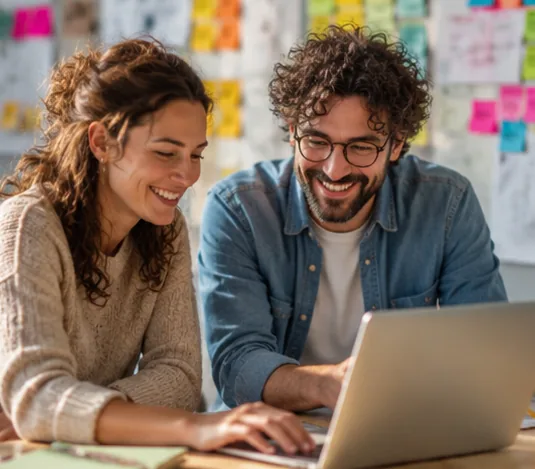 Two colleagues smiling as they work together at a laptop in a bright, colourful office